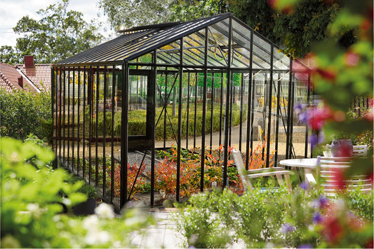 Euro Maxi Special Gewächshaus in Schwarz mit schmalen Scheiben in einem blühenden Garten